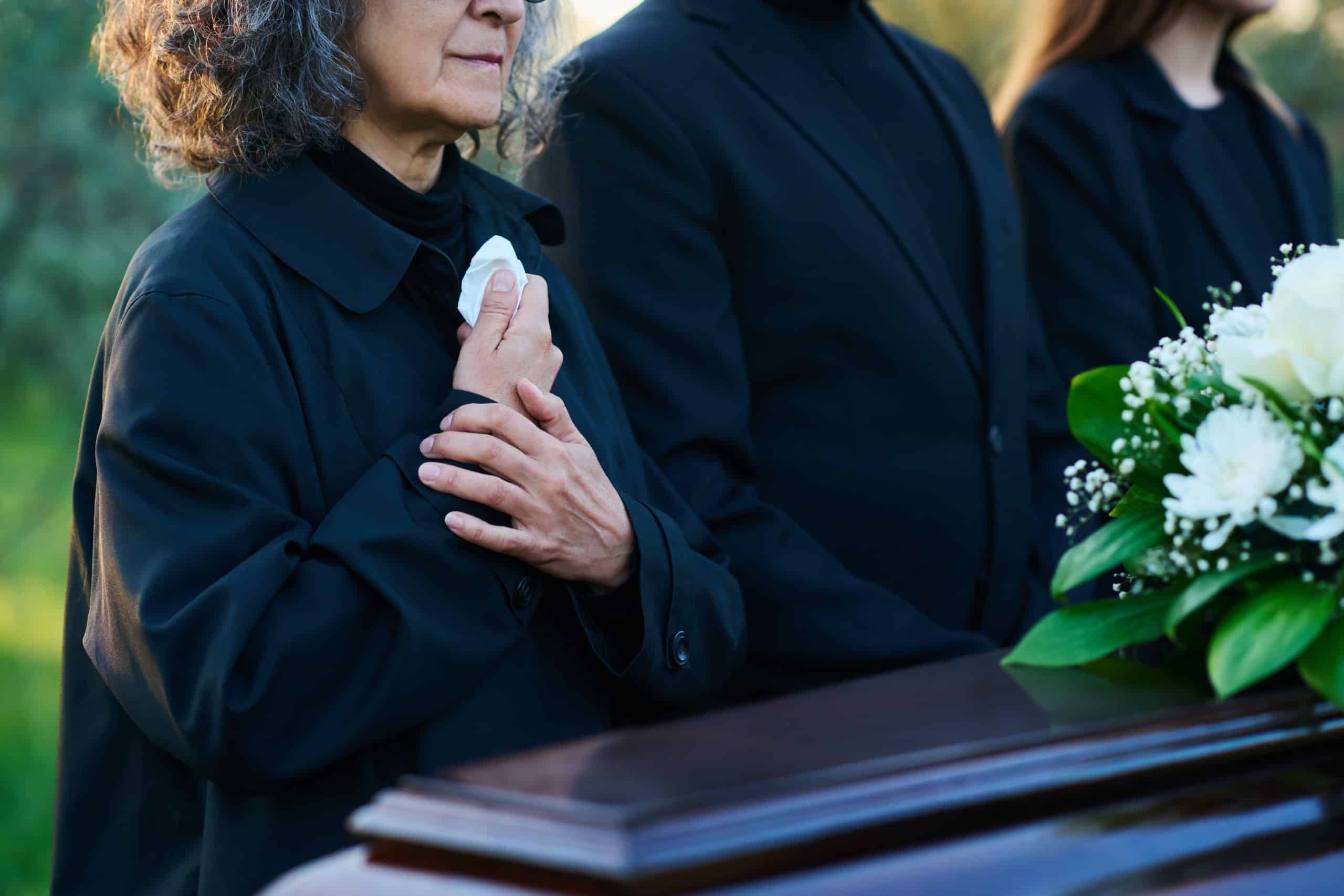 Close up of people standing by a casket at a funeral.