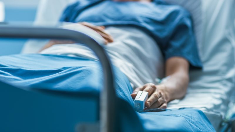 Close up of a patient lying in a hospital bed with a pulse monitor on their finger.