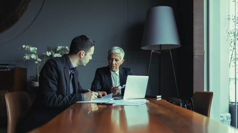 Two lawyers talking and reviewing documents at a conference table.