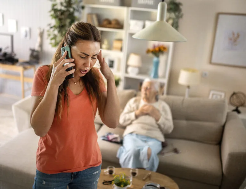 Distressed woman making a phone call while an elderly woman sits in the background.