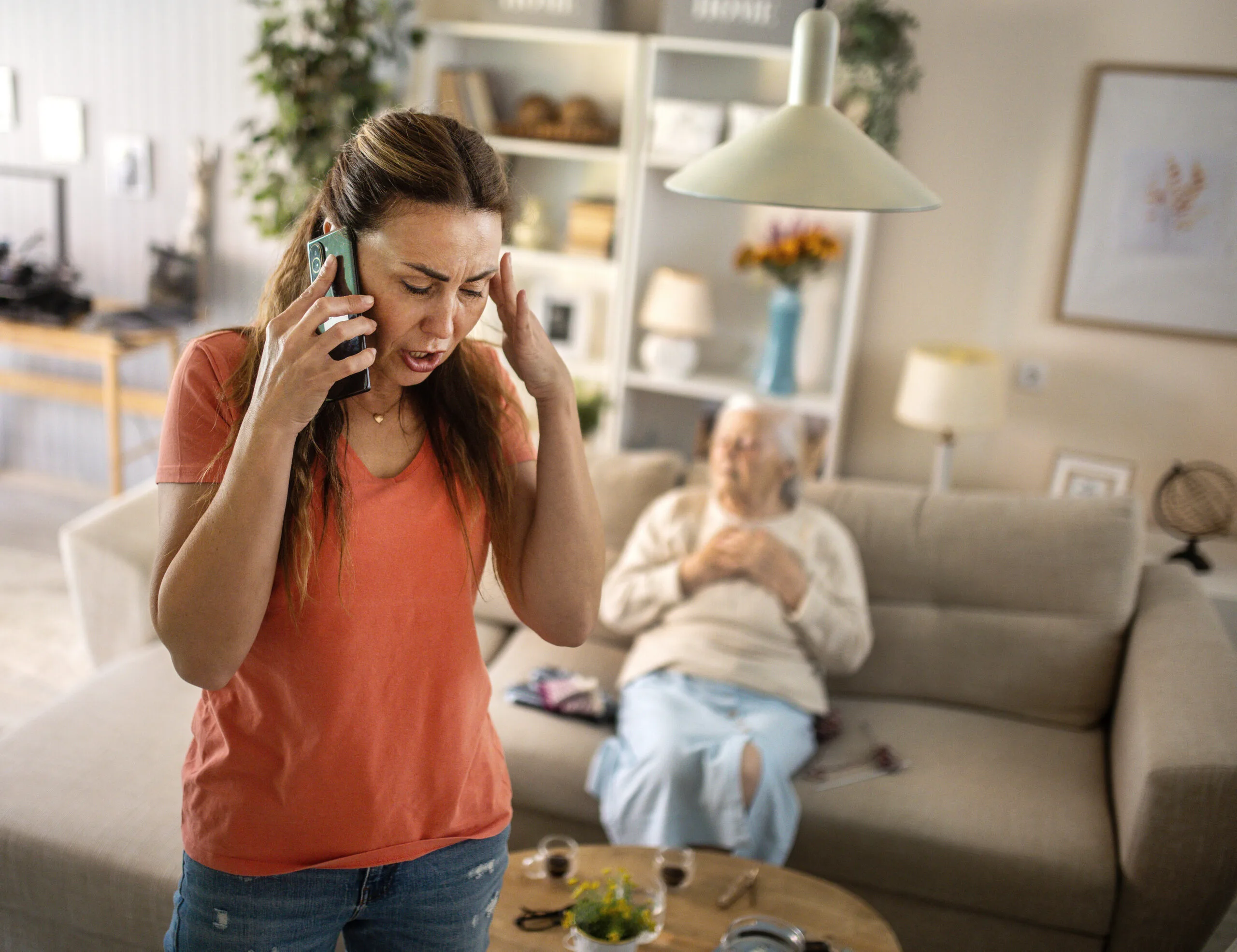 Distressed woman making a phone call while an elderly woman sits in the background.