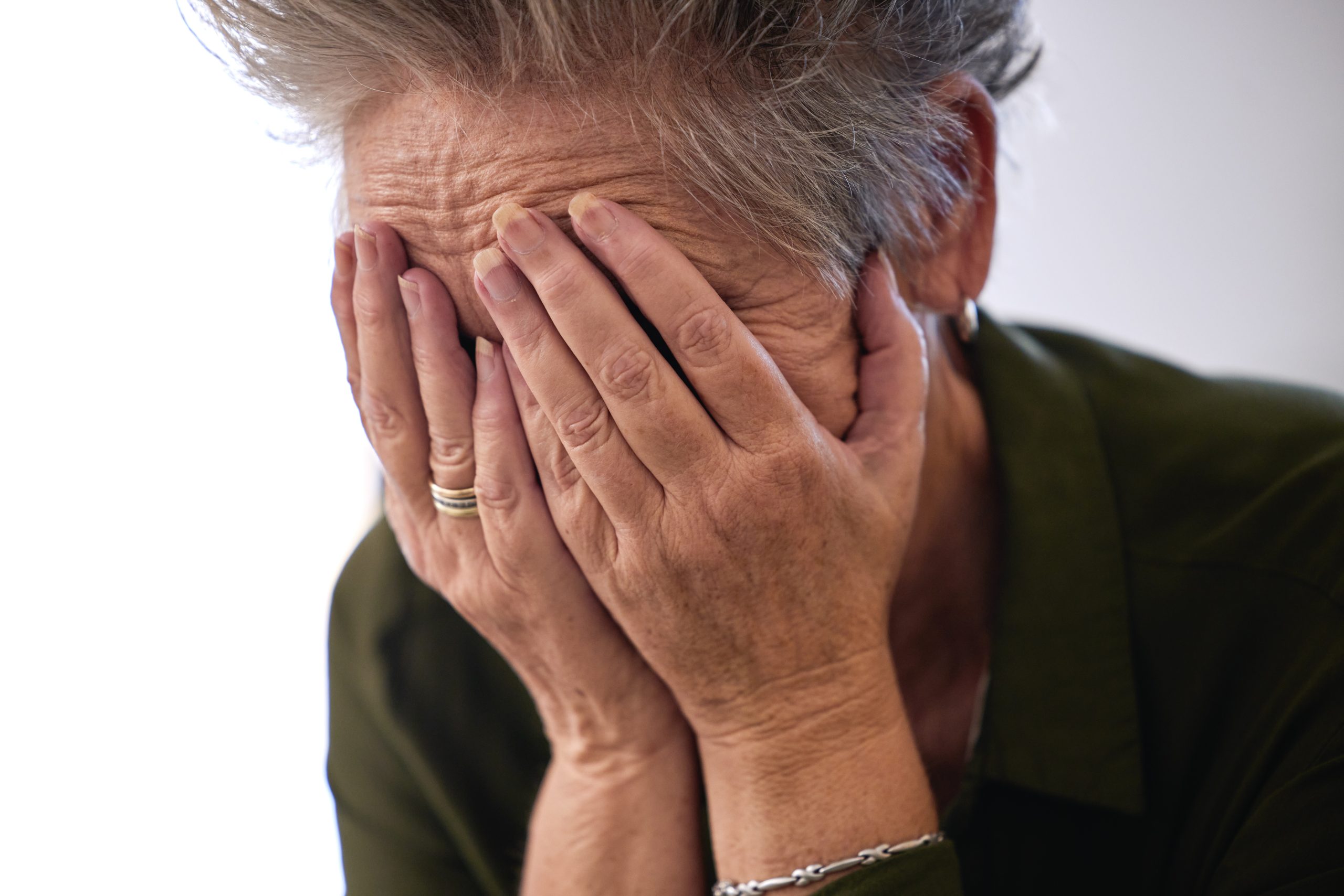 An elderly woman covering her face with both hands.