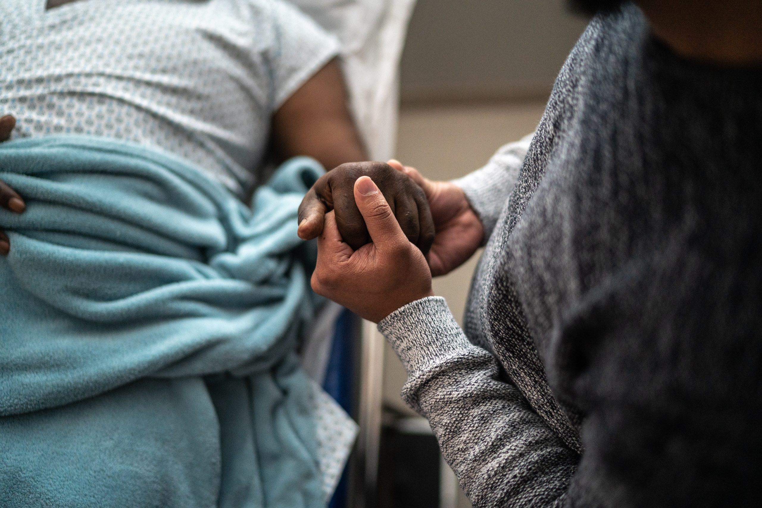 A close-up image of a person holding the hand of a hospital patient.