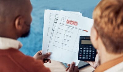A person holding financial documents with a "Payment Required" stamp while another person uses a calculator.