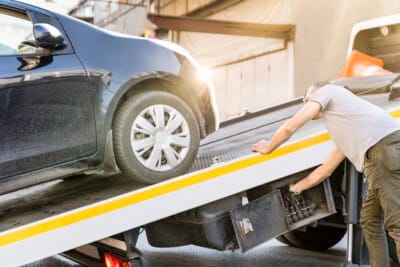 A tow truck operator loads a black car onto a flatbed truck.
