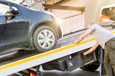 A tow truck operator loads a black car onto a flatbed truck.