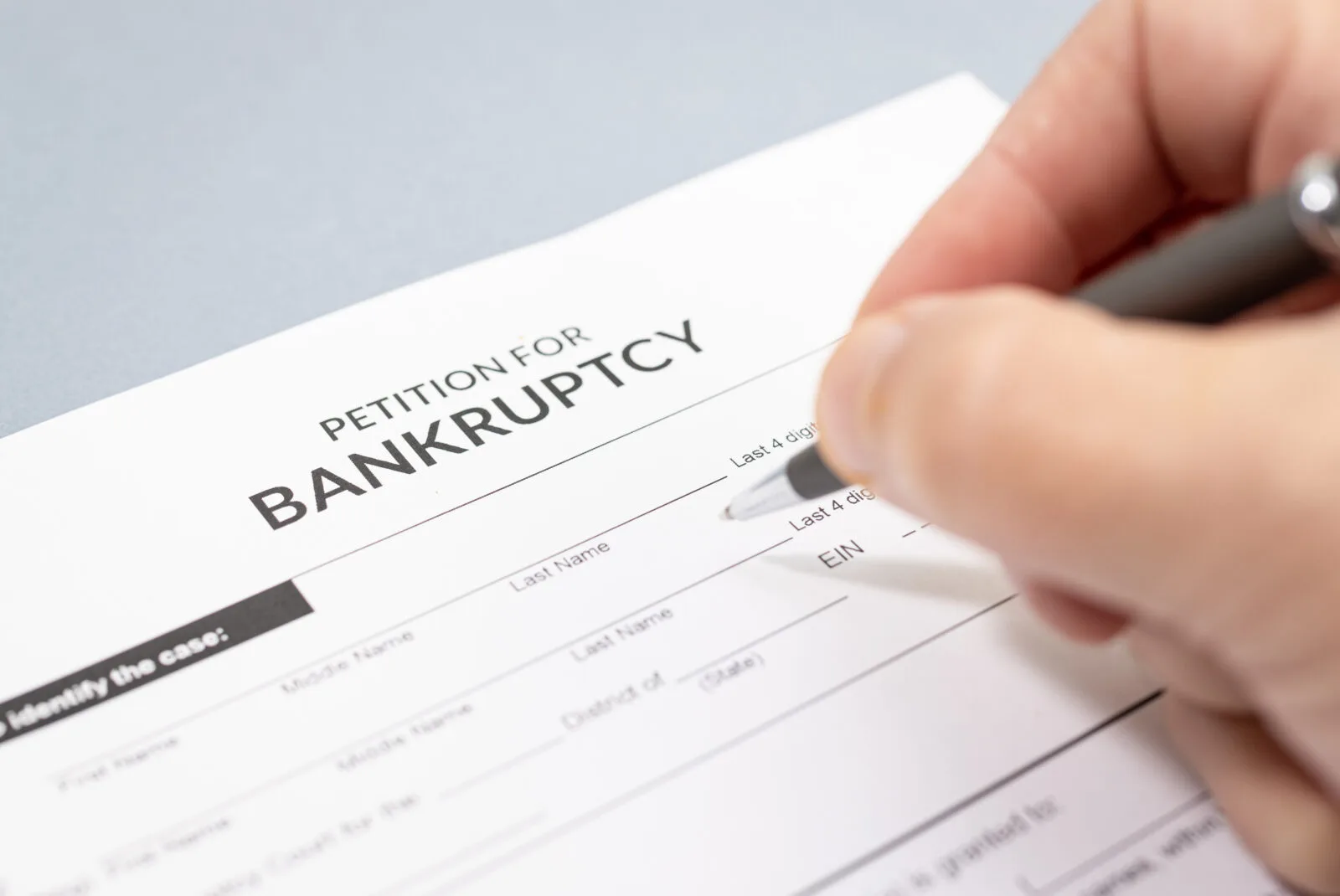 Close-up of a person filling out a petition for bankruptcy form with a pen.