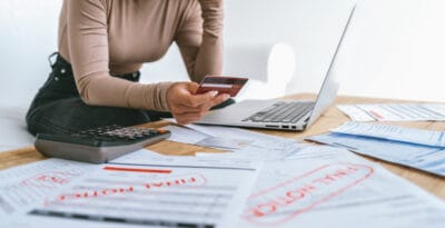 A woman reviews bills and final notices while holding a credit card and using a laptop.