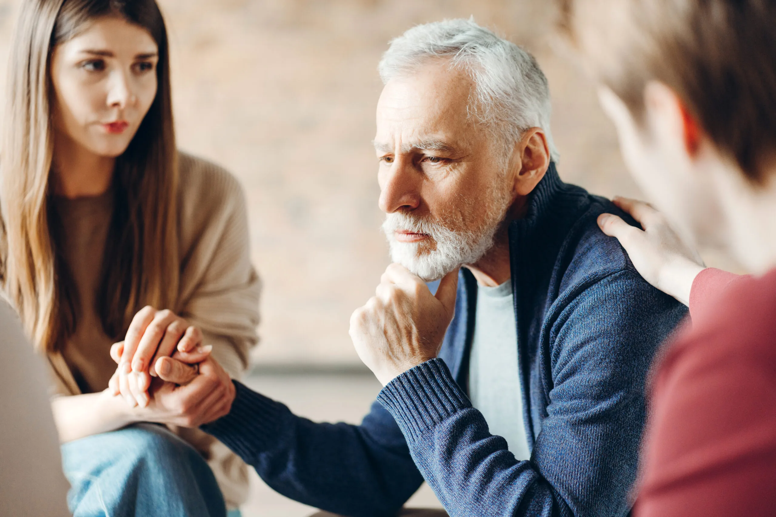 An elderly man looks worried while being comforted by two younger people.